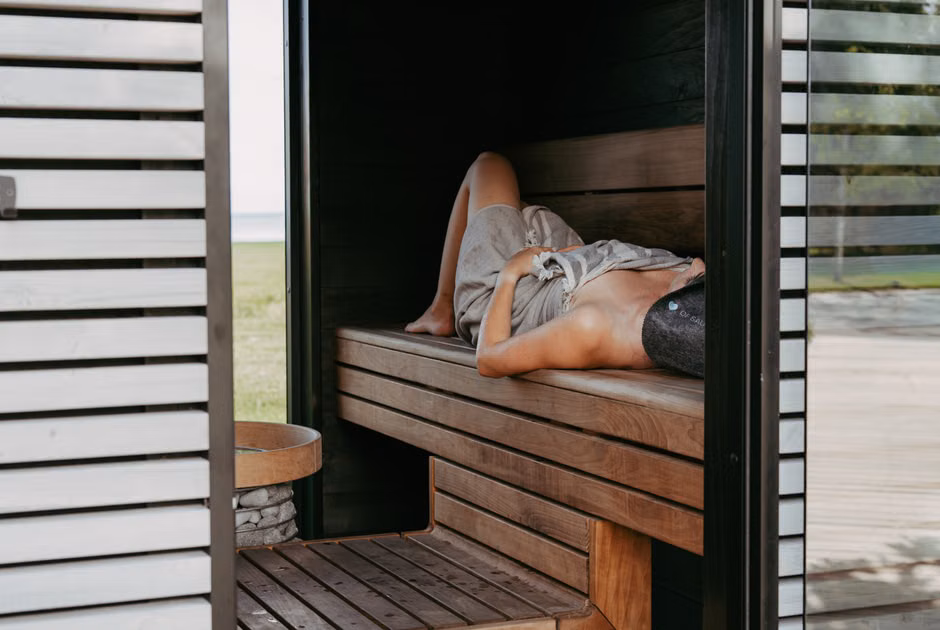 Person relaxing inside a modern sauna with Nordic design, lying with a towel and sauna hat for wellness.