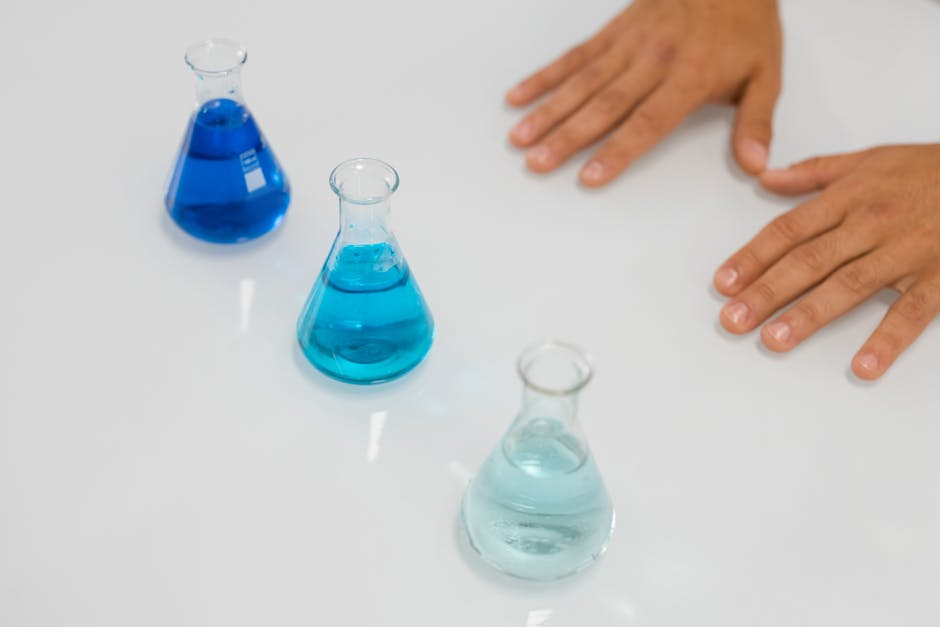 blue liquids in erlenmeyer flasks on a lab table with hands